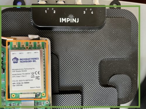 FS-GM704 module mounted on a PCB next to the larger Impinj R700 reader housing, showing the module’s compact form factor.